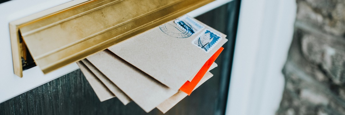 A stack of white letters with stamps being posted through the letterbox of a door. Erin International provide an address verification service.